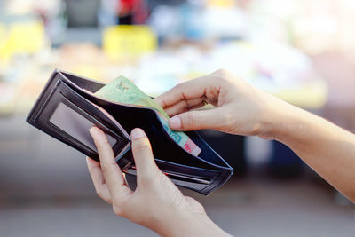 Close-up of woman holding removing money from wallet outdoors