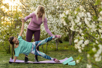 Family mother teacher training yoga child daughter on a yoga mat at home garden. family outdoors. 