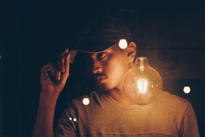 Man wearing cap while light blub reflecting on glass