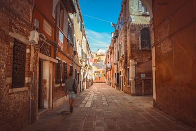 Rear view of man walking in alley amidst buildings in city