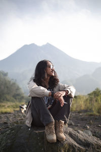 Young woman sitting on mountain against sky