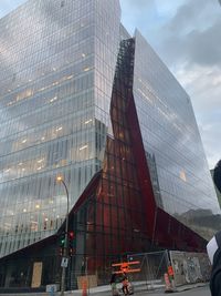 Low angle view of modern glass building against cloudy sky