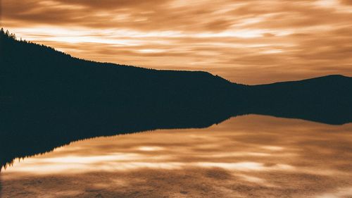 Scenic view of lake by mountains against sky during sunset