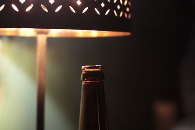 Close-up of beer bottle by illuminated electric lamp at home
