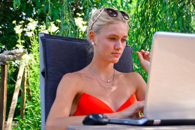 Young woman using laptop while sitting against plants in yard