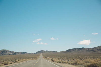 Empty road amidst landscape leading towards mountains against sky