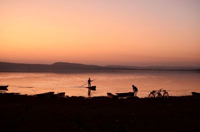 Silhouette man standing on sea against sky during sunset