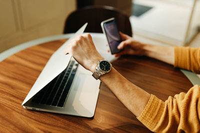 Male human hands hold wireless headphones mobile phone and laptop on a wooden desk in the workplace