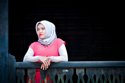 Portrait of young woman standing against window