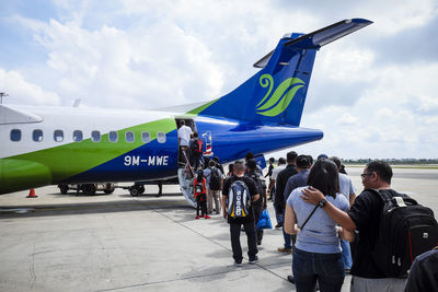 Rear view of people at airplane against sky