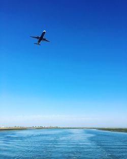 Low angle view of man flying over sea against clear blue sky