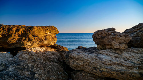 Scenic view of rocks in sea against clear blue sky