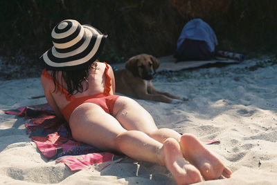 Midsection of woman with dog relaxing on sand at beach