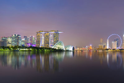 Illuminated city by river against sky at night