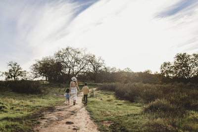 Young mother, son, and daughter holding hands while walking away