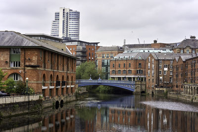 Bridge over river by buildings in city against sky