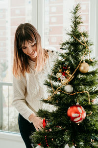 Smiling young woman standing by christmass tree at home