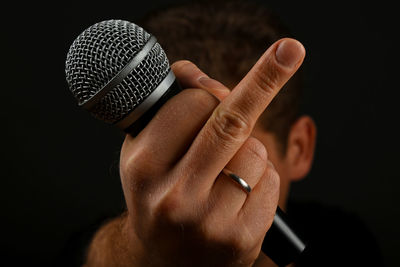 Cropped hand of man holding microphone while gesturing against black background