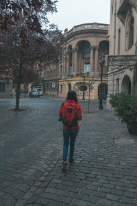 Rear view of woman standing on footpath by building