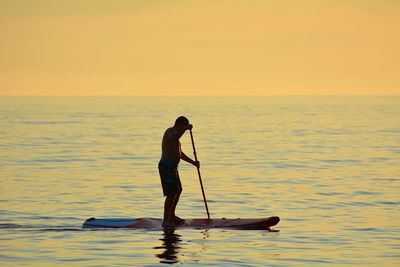 Man paddleboarding on sea during sunset