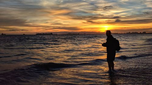 Silhouette person standing on beach against sky during sunset