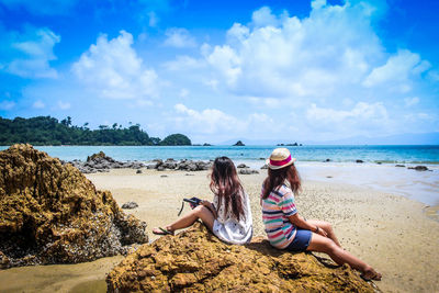 Woman sitting on rock at beach against sky