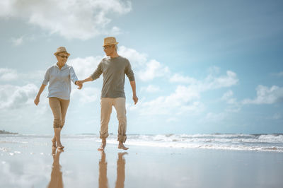Couple holding hands while walking at beach against sky