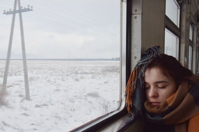 Woman sleeping by window in train during winter