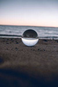 Close-up of crystal ball on beach against sky during sunset