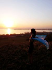 Rear view of woman standing on field against sky during sunset