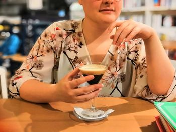 Midsection of young woman drinking glass on table at restaurant