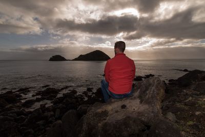 Rear view of man standing on rock by sea against sky