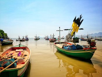 Fishing boats moored at harbor against sky