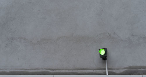Green traffic light in front of the gray wall