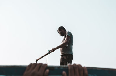 Low angle view of man holding pipe against clear sky