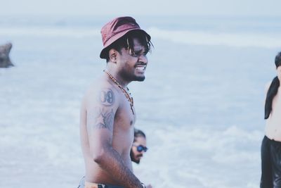 Side view of shirtless smiling young man standing at beach
