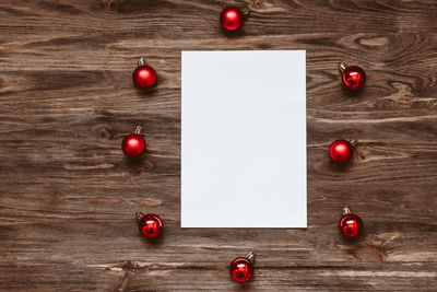 A blank sheet of paper and and red christmas balls on a wooden background. top view, flat lay