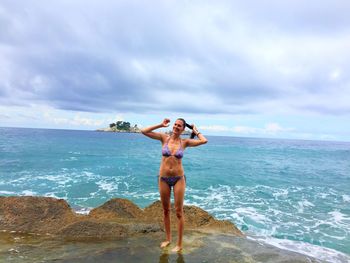 Full length portrait of woman in bikini standing at beach against sky