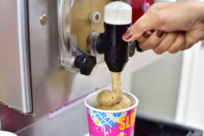 Close-up of hand using ice cream machine while filling cup at shop
