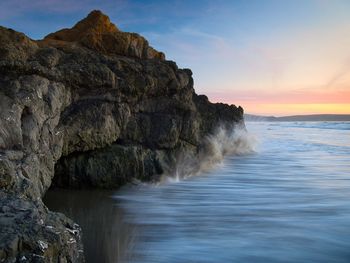 Rock formation in sea against sky during sunset