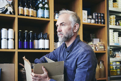 Mature salesman looking away while working in deli