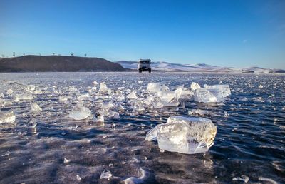 Vehicle on frozen lake beikal against clear blue sky during sunny day