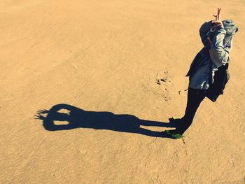 High angle view of playful woman standing by shadow on sand at beach