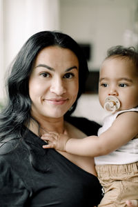 Portrait of smiling mother carrying son at home