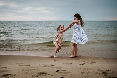 Older sister swinging younger sister on the beach at lake michigan