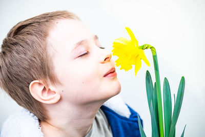 Close-up of boy with yellow flower against white background
