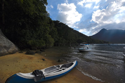 Boats moored on sea by mountain against sky