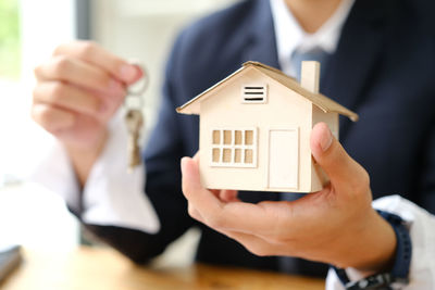 Midsection of businessman holding model house in office