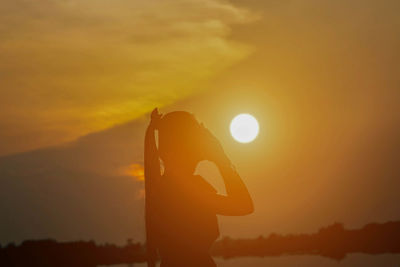 Silhouette woman standing against orange sky during sunset