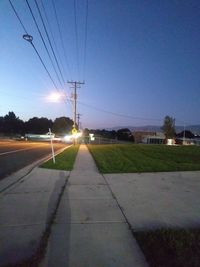 Road by illuminated city against sky at dusk